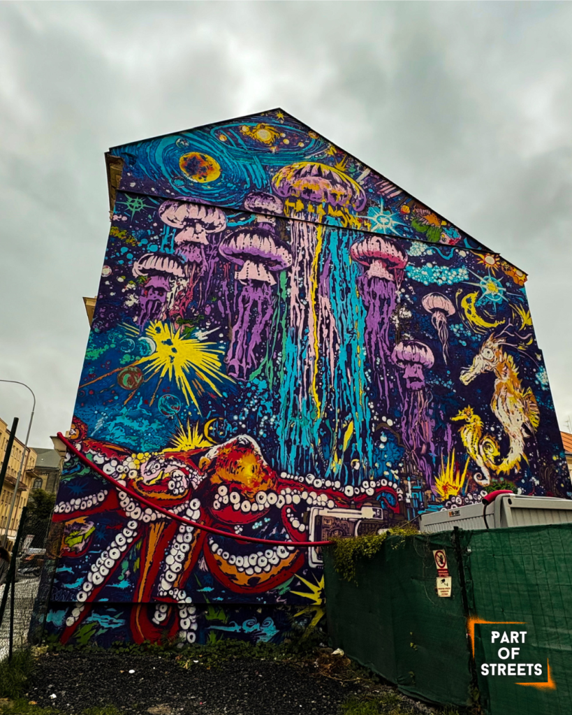 Vibrant street art mural of jellyfish, sea creatures, and an octopus in a cosmic underwater scene on the side of a building in Prague.