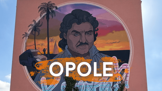 A stylized mural portrait of a man with dark curly hair and a mustache set against a sunset background with palm trees. The word “OPOLE” appears in bold white letters on the right side of the image.