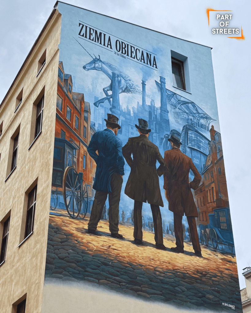 Street art mural in Łódź inspired by “Ziemia Obiecana” (The Promised Land), showing three men in old-fashioned coats looking at industrial Łódź with factory chimneys in the background. Painted by Maciej Bielewicz to celebrate 50 years of the iconic Polish film.