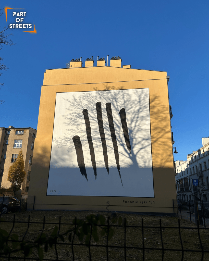 Mural “Podanie Ręki ’81” by Józef Robakowski in Łódź, minimalist hand symbol inspired by his 1981 “Handshake” action.
