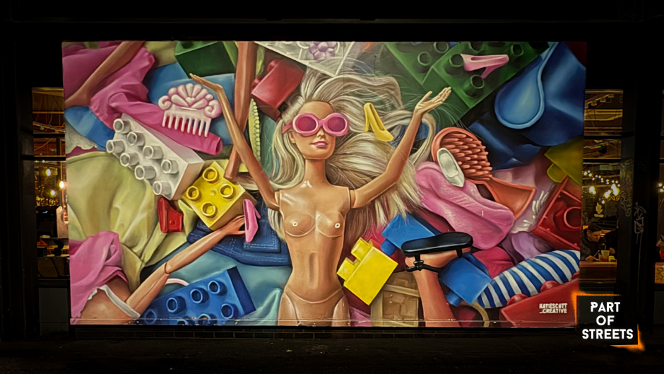 Large colourful mural by Katie Scott in Manchester Northern Quarter depicting a Barbie-like figure surrounded by plastic objects and toys.